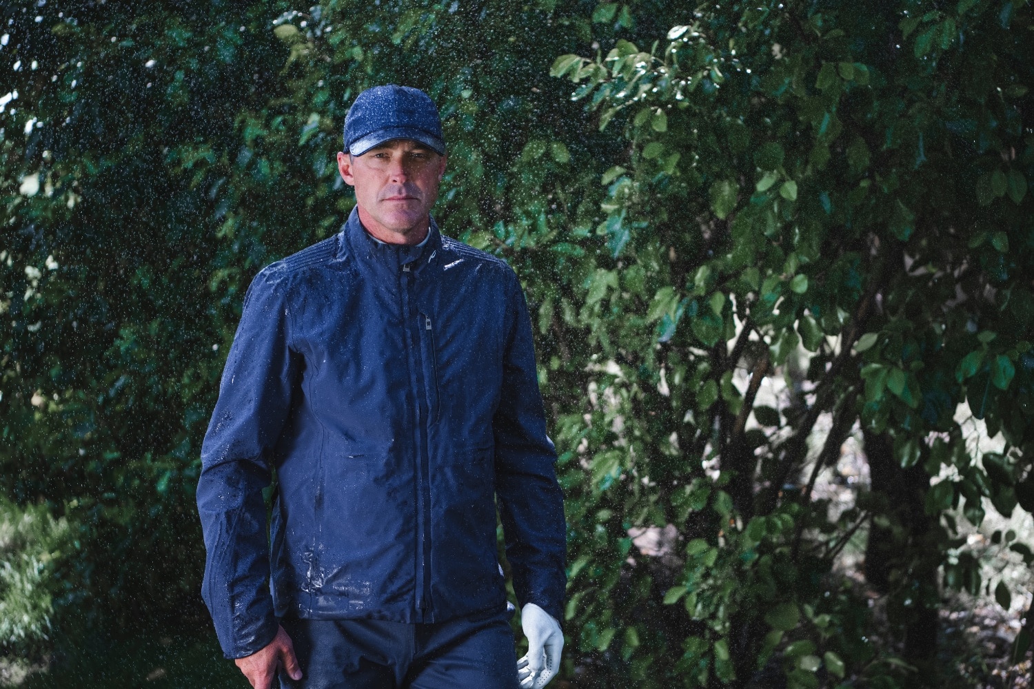 A man wearing a navy blue KJUS rain jacket in the rain.