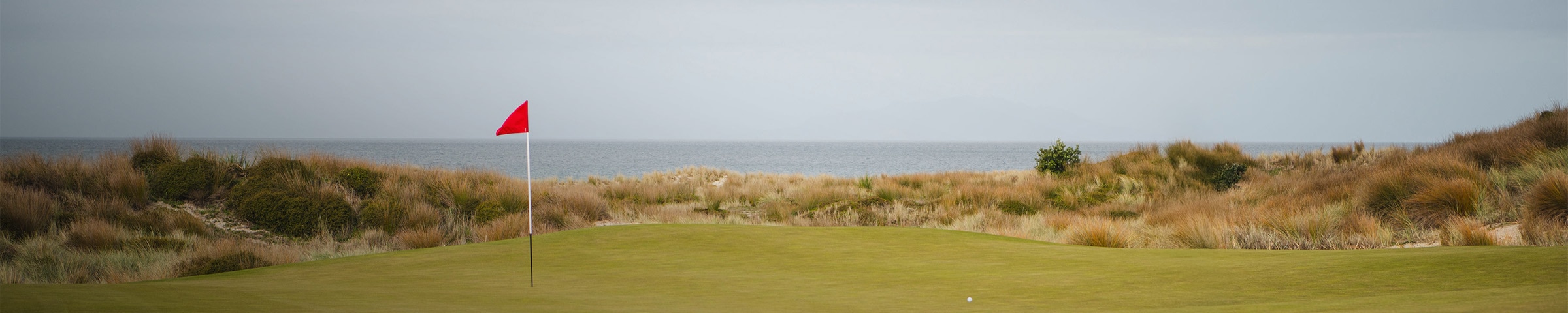 A woman wearing a KJUS cap looks out over the golf course, large cliffs and vegetation behind her.