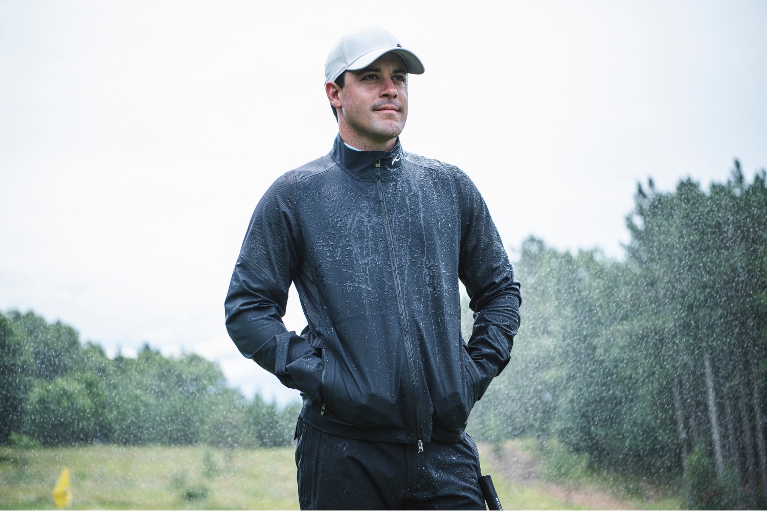A male golfer in the KJUS Pro 3L 3.0 Jacket is standing in the rain.
