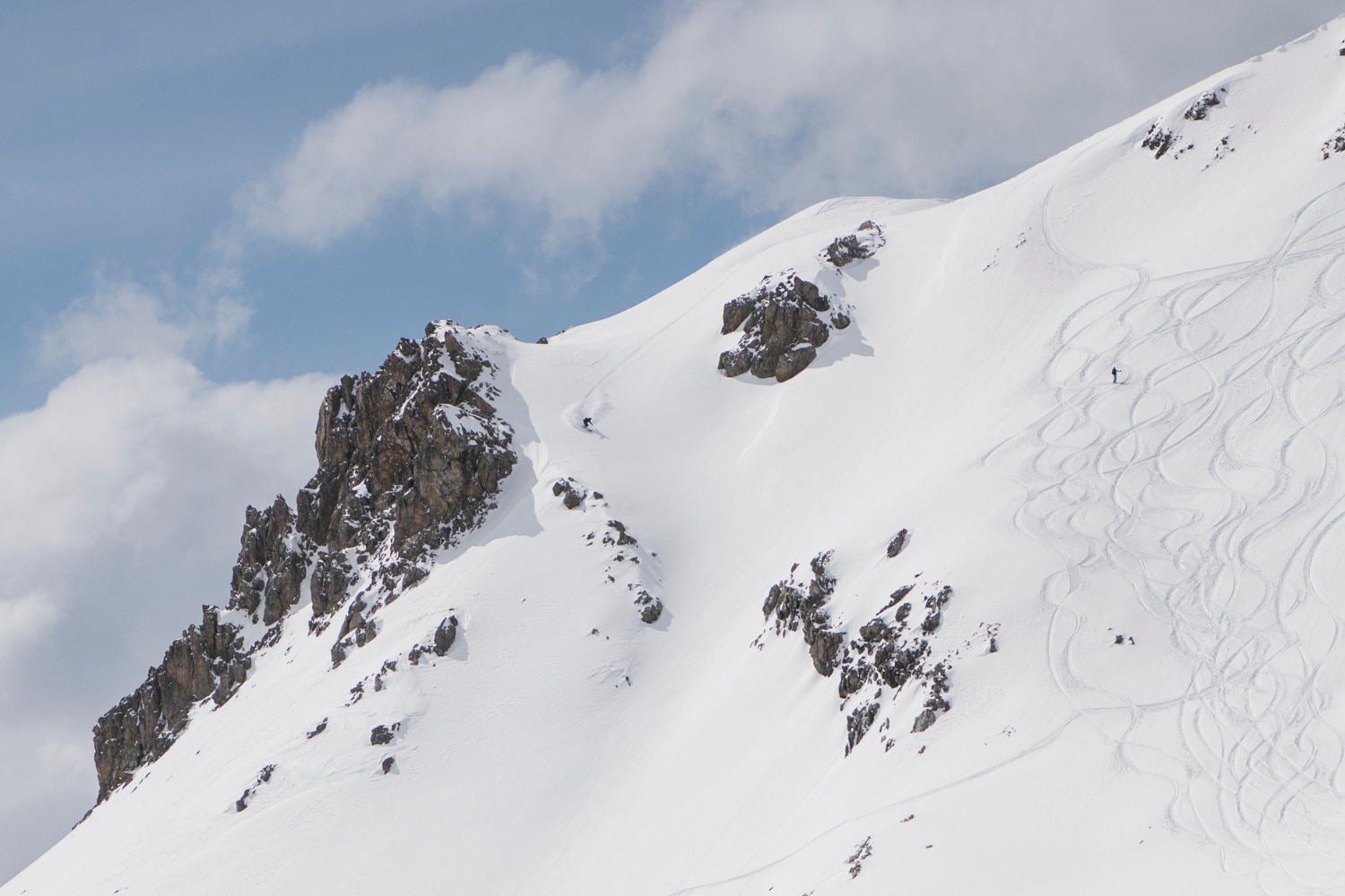 Two skiers can be seen skiing down a snow-covered mountain slope. 