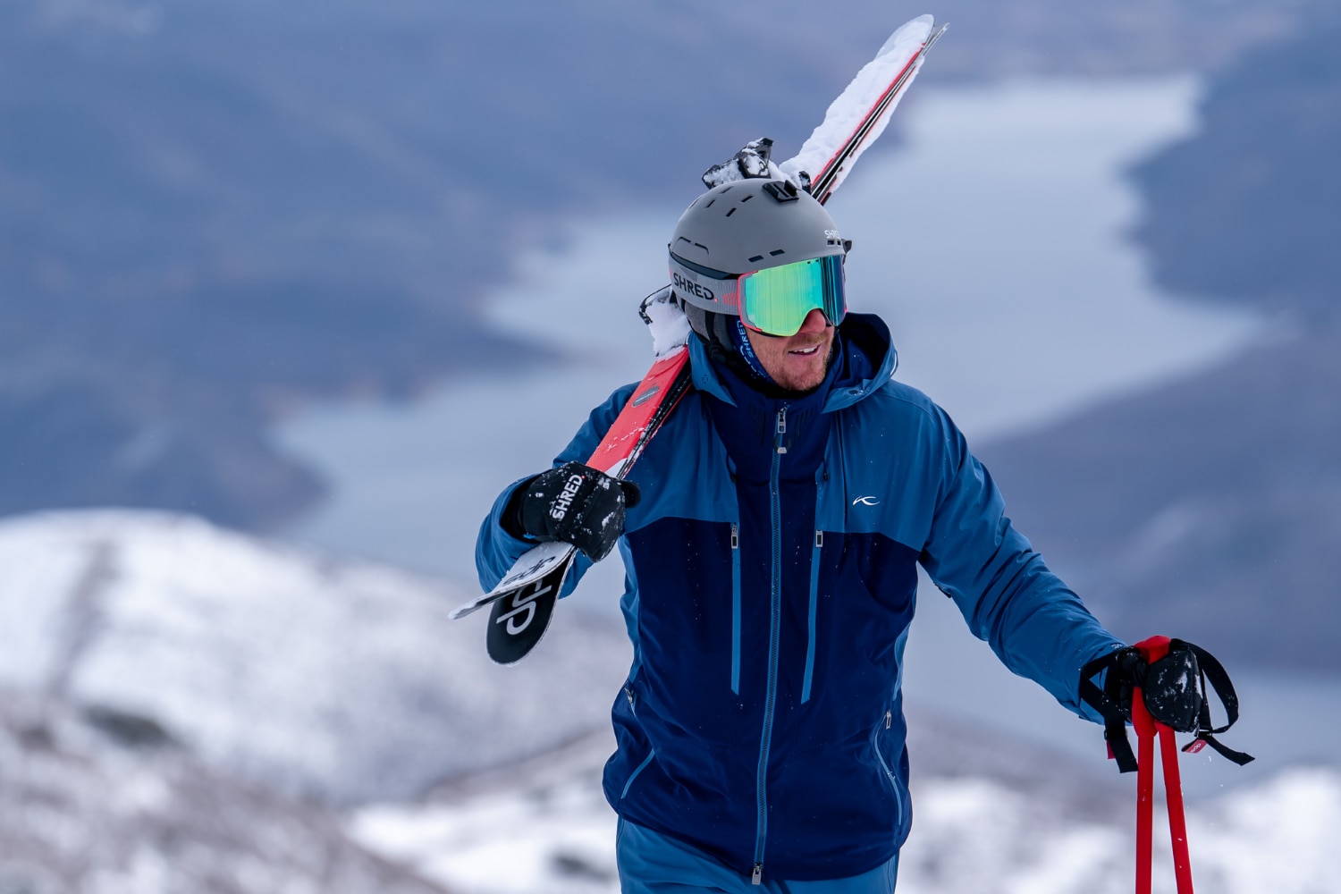 A skier in blue KJUS outfit is carving down a slope, some trees in the backgorund.