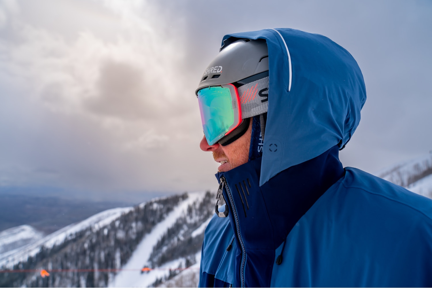 Two skiers in blue KJUS ski outfits high-fiving each other on a slope, snowy peaks in the background.