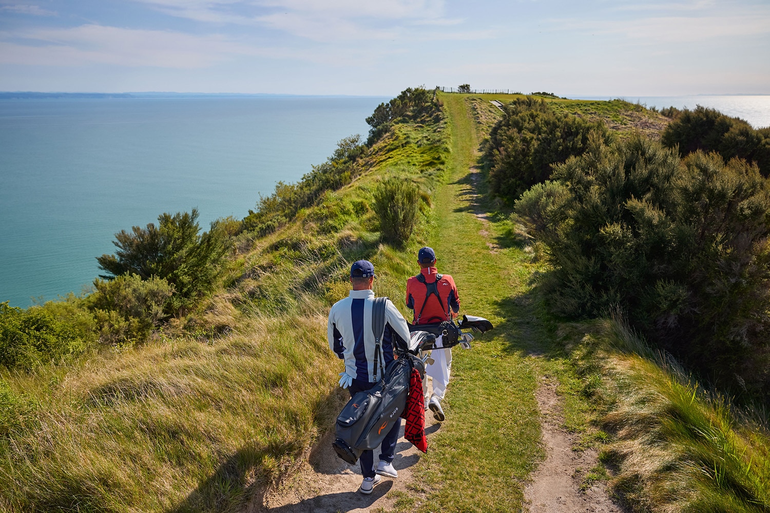 Two golfers walking along a coastline on the golf course wearing KJUS golf apparel.
