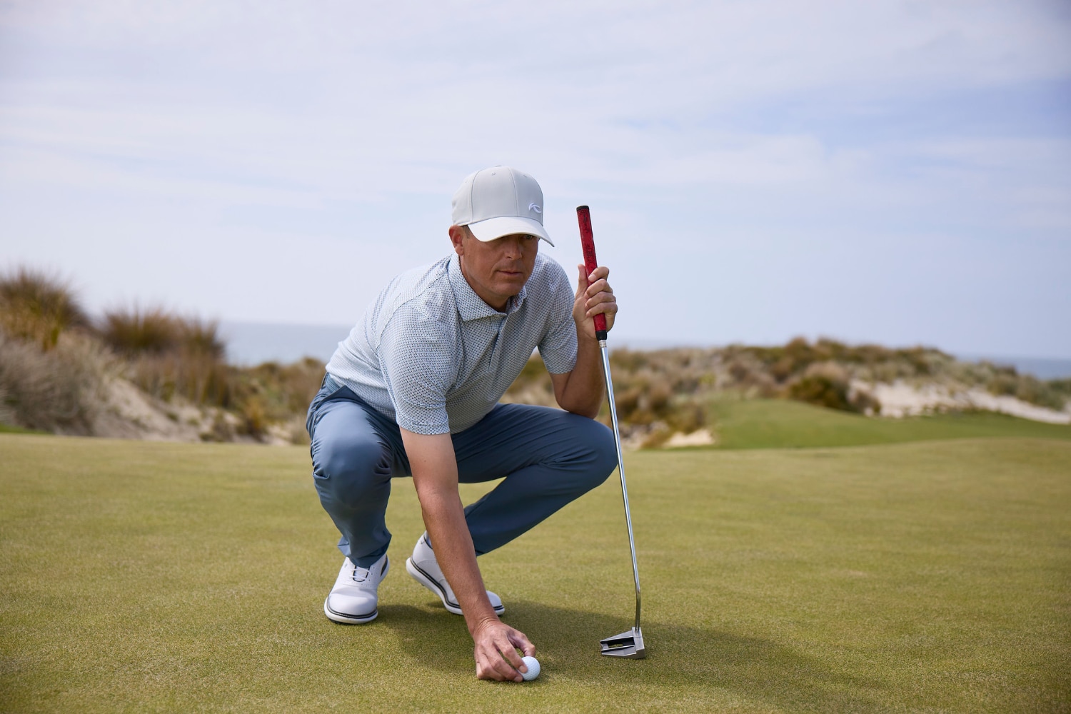 A male golf player crouching on the green, placing a golf ball.