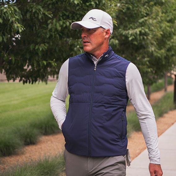Man wearing a navy KJUS insulator vest with a long sleeve polo and a cap